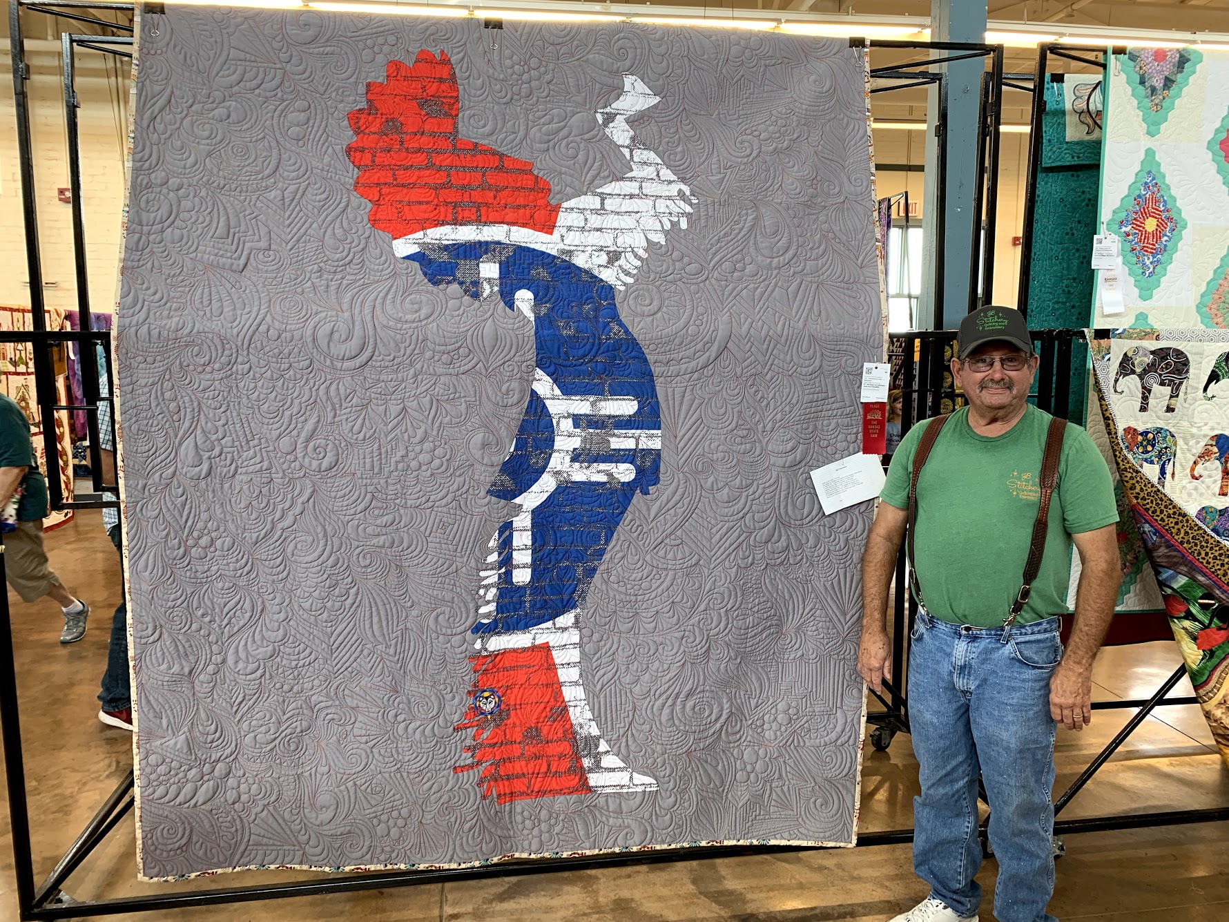 Bob Callstrom standing next the red ribbon quilt that was submitted in the 2019 Kansas State Fair.